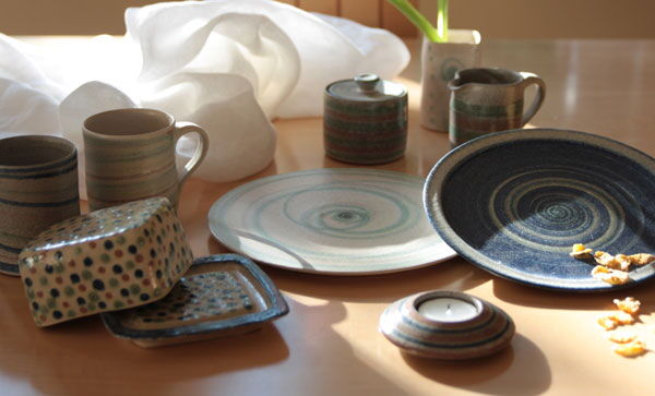 Gedeckter Tisch mit Tassen, Tellern, Butterdose und Kerzenhalter